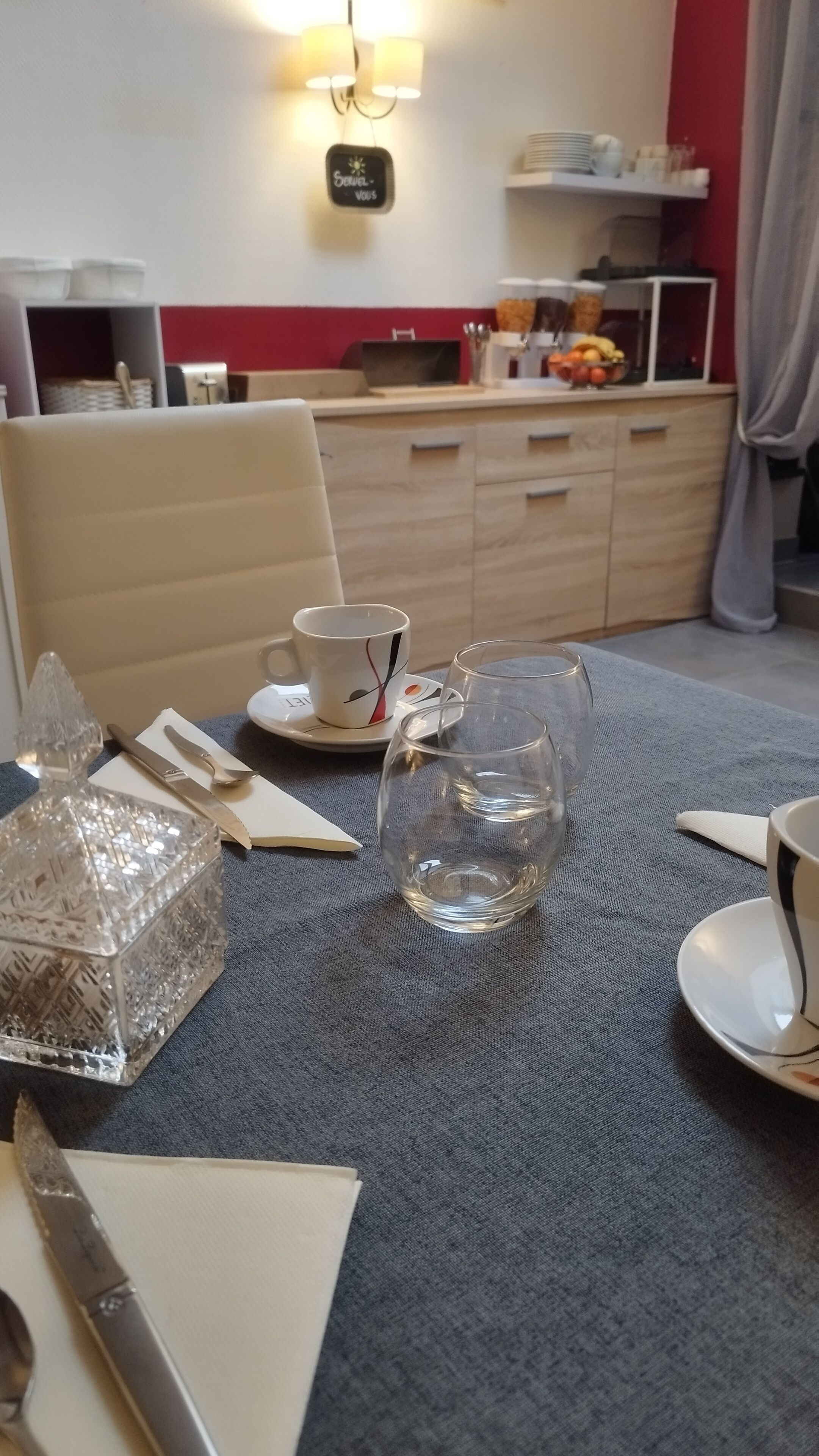 A dining area with a table set for two, featuring a clear glass, a white cup, and a crystal decanter.