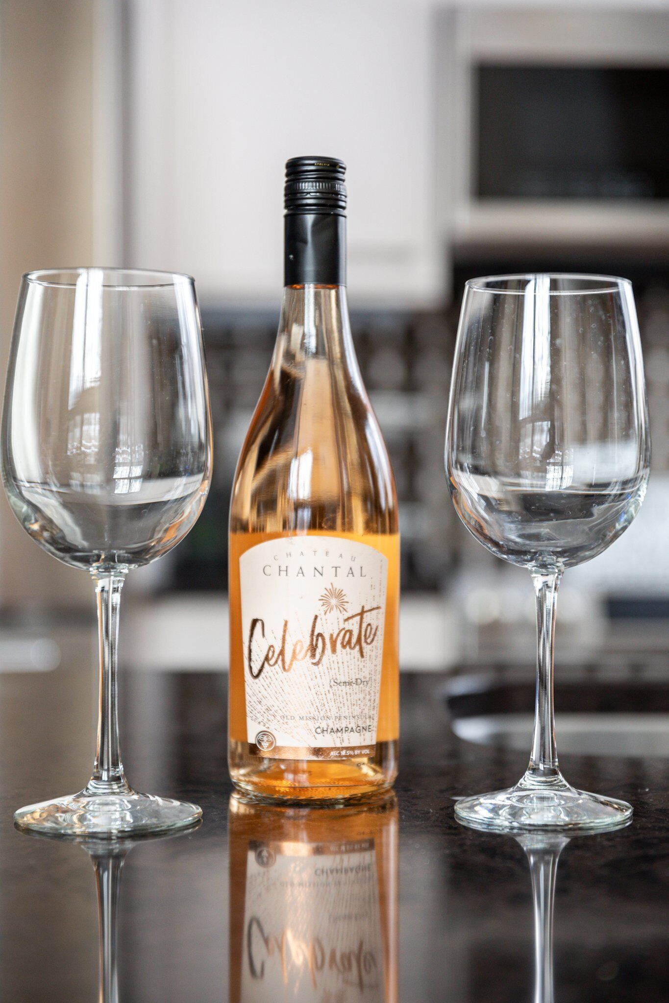 A bottle of Chateau Chantai Celebrator champagne and two empty wine glasses on a reflective surface.
