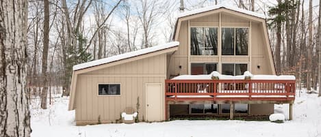 A two-story cabin with a red balcony, surrounded by a snowy forest.