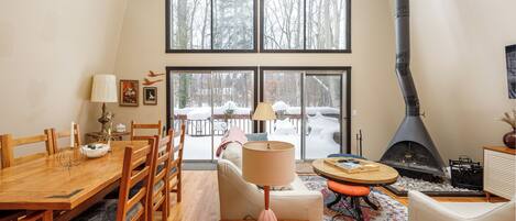 A cozy living room with a fireplace, wooden furniture, and large windows overlooking a snowy landscape.