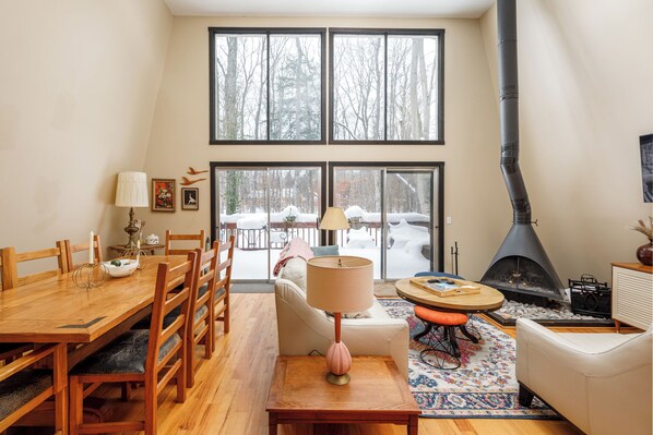 A cozy living room with a fireplace, wooden furniture, and large windows overlooking a snowy landscape.