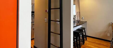 Un interior moderno con piso de madera, una escalera con barandillas negras y una cocina visible al fondo.