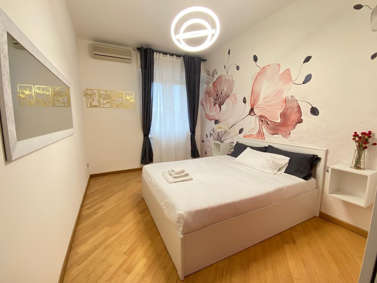 Une chambre à coucher comprenant un lit, un climatiseur fixé au mur, un luminaire au plafond et une fresque murale à motifs floraux.