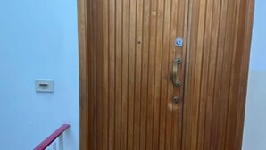 A wooden door with a metal handle and a peephole, a white railing, and a brown doormat with paw prints.