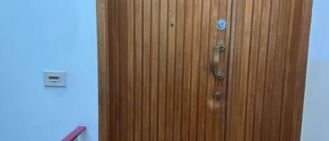 Una puerta de madera con un picaporte de metal y un ojo de buey, una barandilla blanca y un felpudo marrón con huellas de patas.