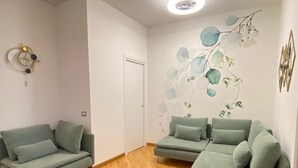 A modern living room with two green sofas, a wooden floor, and a wall with a leaf pattern.