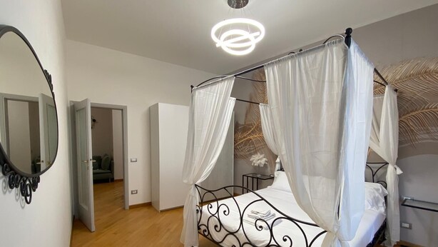 A four-poster bed with white bedding, a round mirror on the wall, and a modern ceiling light fixture.