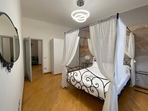 Un lit à baldaquin avec une literie blanche, un miroir rond accroché au mur et un luminaire moderne au plafond.