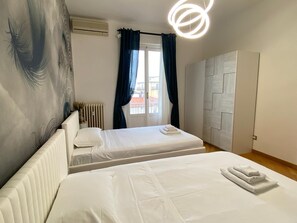 Une chambre d’hôtel avec deux lits, un radiateur, une fenêtre avec des rideaux, une armoire blanche et un luminaire moderne.