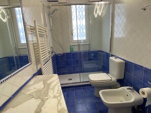 Une salle de bain équipée d’une douche, de toilettes, d’un bidet et d’un plan de toilette en marbre.