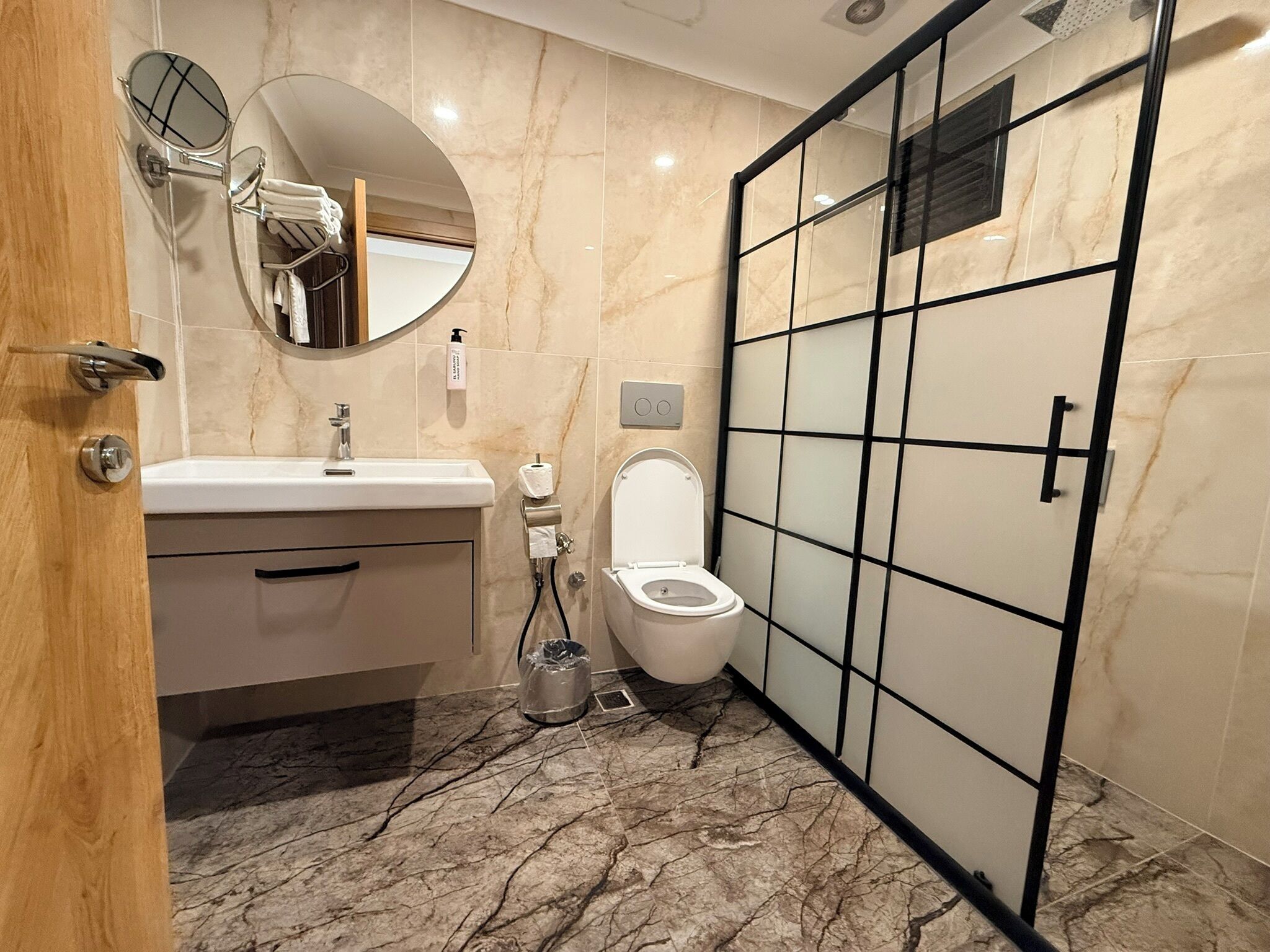 A modern bathroom with a marble floor, a white sink, a toilet, a mirror, and a shower enclosure.