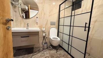 A modern bathroom with a marble floor, a white sink, a toilet, a mirror, and a shower enclosure.
