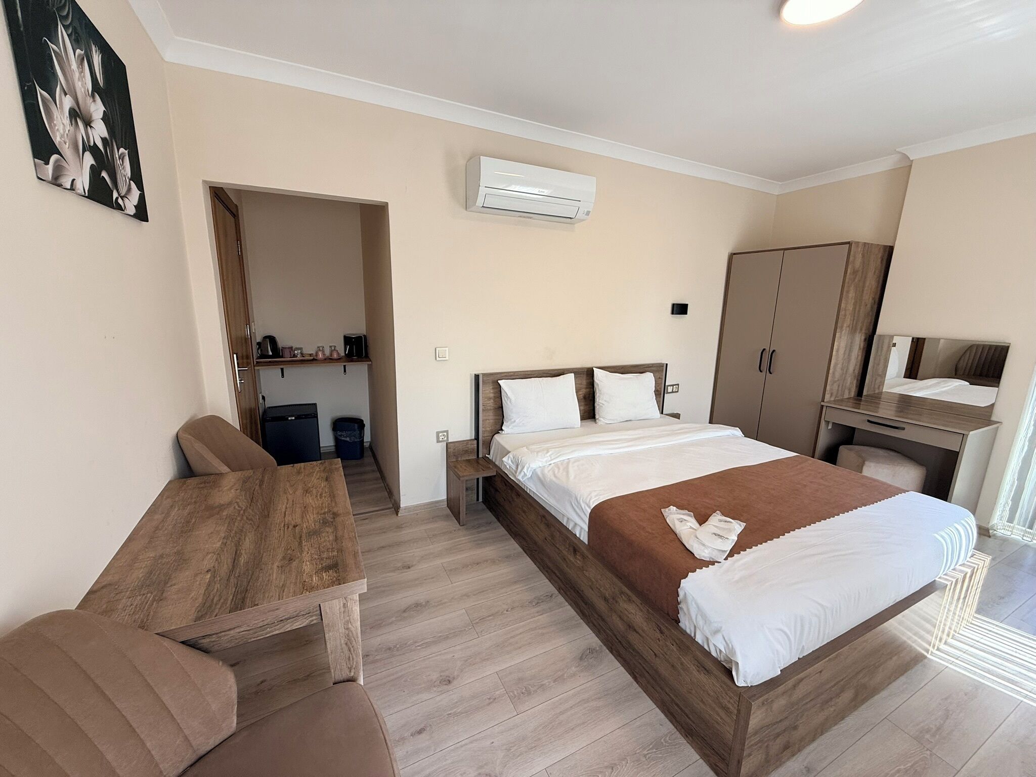 A hotel room with a bed, a desk, a chair, a wardrobe, and an air conditioning unit.