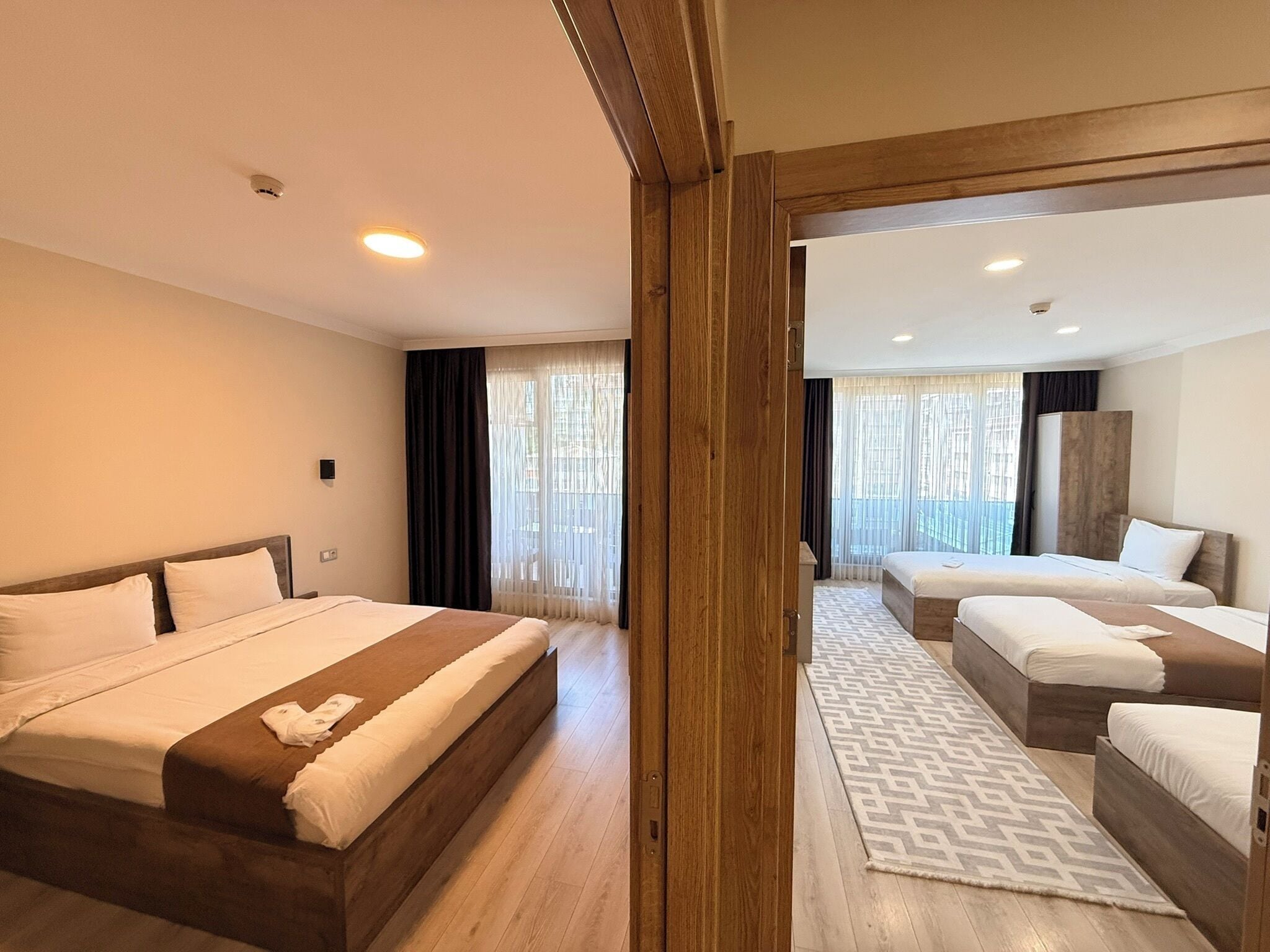 Ein Hotelzimmer mit einem großen Bett, zwei Einzelbetten, Holzboden und Blick durch eine Glastür.