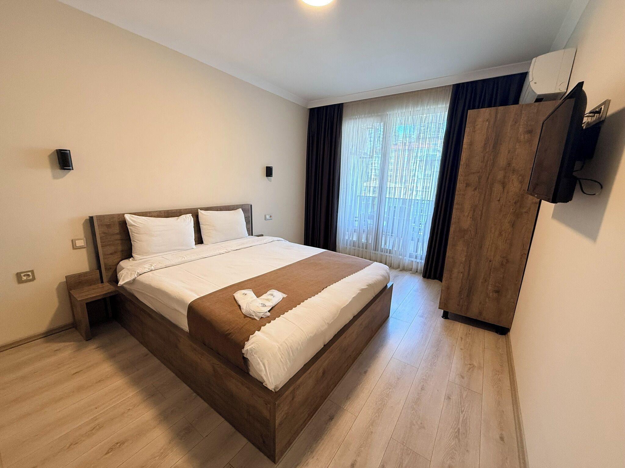 A hotel room with a wooden bed, a nightstand, a wardrobe, and a window with curtains.