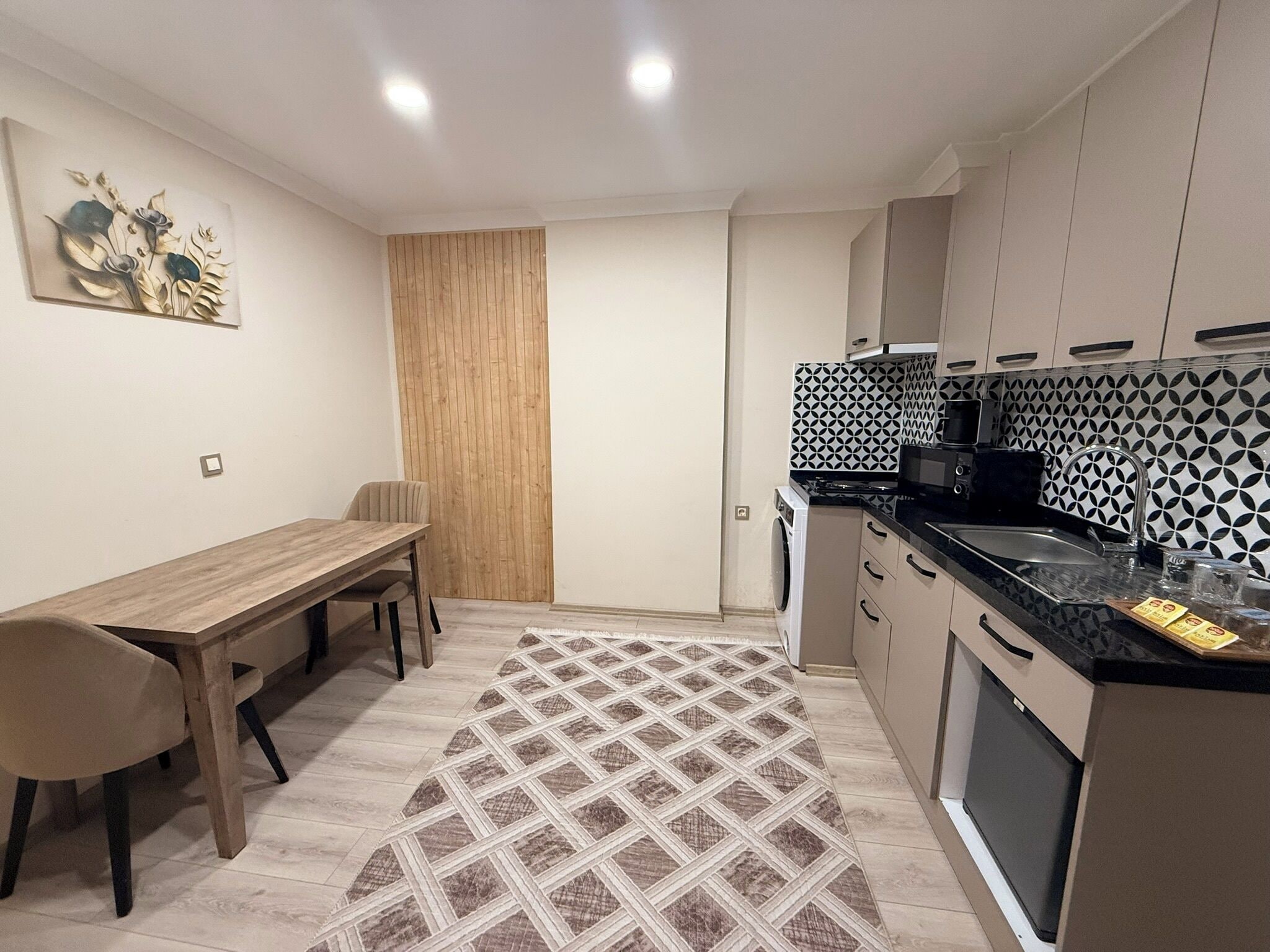 A compact kitchen with a dining area, a washing machine, and a patterned rug.