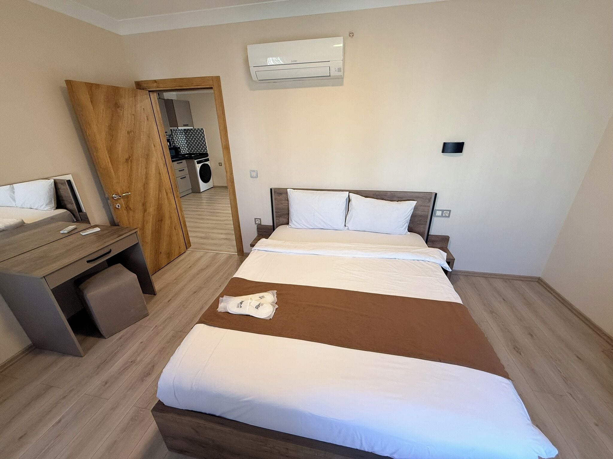 Habitació d'hotel amb un llit, un escriptori, una cadira, un aparell d'aire condicionat i una porta que dóna a una zona de bugaderia.