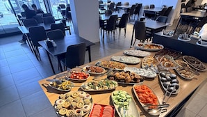A buffet with various food items, a seating area with tables and chairs, and a view of the outside through large windows. - Rena Grand Residence & Suite (Yomra)