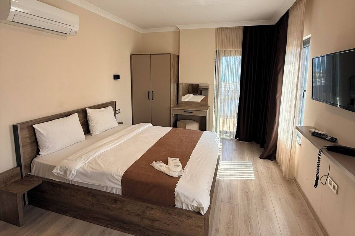 A hotel room with a wooden bed, a wardrobe, a desk, a TV, and an air conditioning unit.