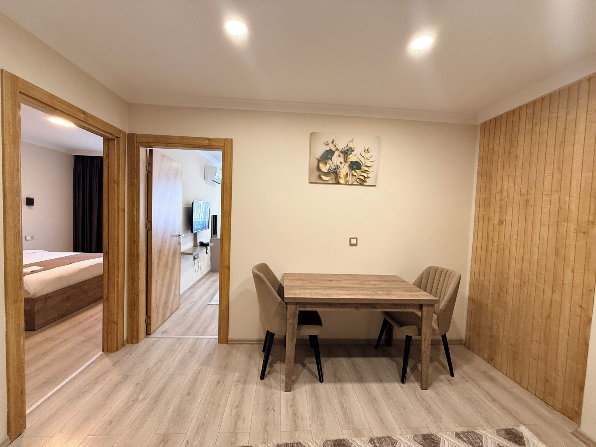 Une pièce comprenant une table à manger en bois, deux chaises, un tableau accroché au mur et une cloison en bois.