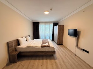 Ein Schlafzimmer mit Bett, Kleiderschrank, Fernseher und einem Fenster mit Vorhängen.
