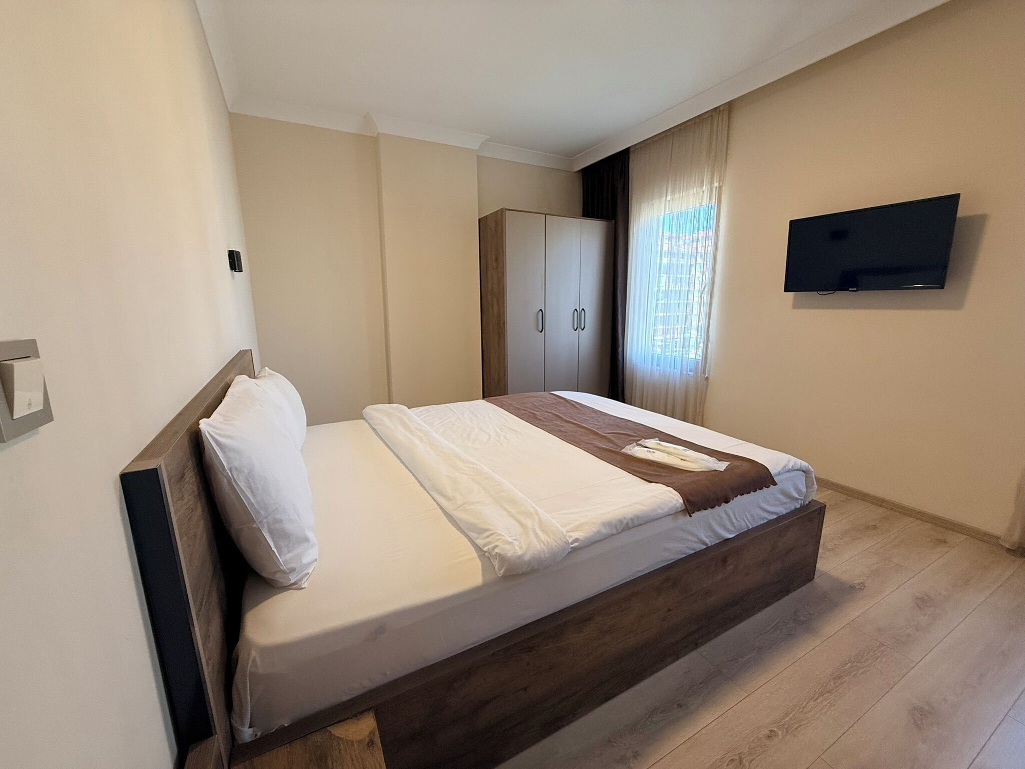 A bedroom with a bed, a wardrobe, a television, and a window with curtains.