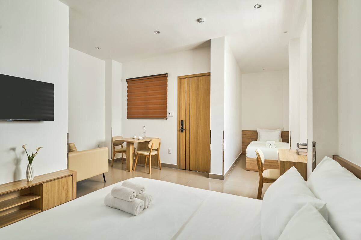 Une chambre d’hôtel moderne avec un grand lit, un bureau, une chaise, une armoire en bois et un téléviseur fixé au mur.