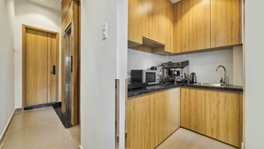 A modern kitchen with wooden cabinets, a built-in microwave, a coffee machine, and a sink. - Mihn Suites Ben Thanh (Ho Chi Minh City)