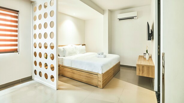 A modern bedroom with a wooden bed frame, white bedding, and a small wooden side table. - Mihn Suites Ben Thanh (Ho Chi Minh City)