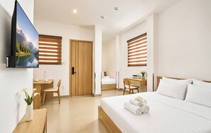A modern hotel room with a large bed, a desk, a chair, a TV mounted on the wall, and a window with blinds. - Mihn Suites Ben Thanh (Ho Chi Minh City)