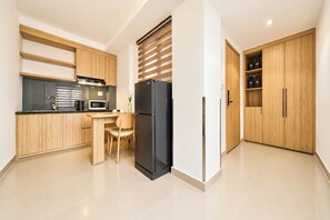 A modern kitchen with wooden cabinets, a black refrigerator, a microwave, and a dining area with a chair. - Mihn Suites Ben Thanh (Ho Chi Minh City)