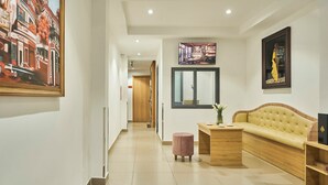 A modern hotel lobby with a long corridor, a sofa, a small table with a vase, and artwork on the walls. - Mihn Suites Ben Thanh (Ho Chi Minh City)