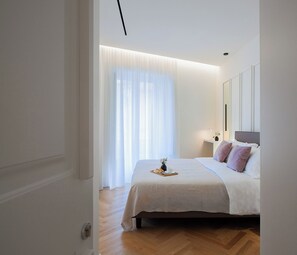 Une chambre à coucher moderne avec un grand lit, une table de chevet avec une lampe et des rideaux légers.