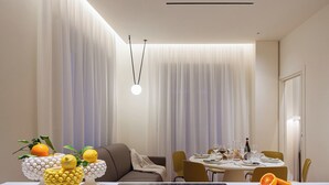 Un comedor moderno con una mesa dispuesta para dos personas, un centro de mesa decorativo con fruta, y una lámpara colgante.