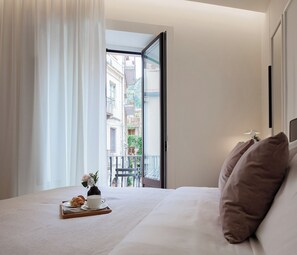 A hotel room with a bed, a tray with croissants and a cup, and a view of buildings through an open door. - Maia Flora Taormina Apartments (Taormina)