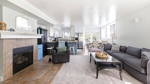 A modern living room with a fireplace, a sofa, a coffee table, and a kitchen in the background. - Lakefront Condo, Only Steps To The Beach (Michigan City)