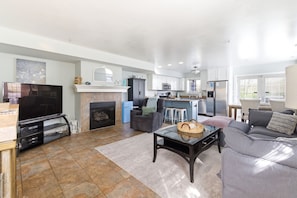 A spacious living room with a fireplace, a television, a sofa, and a kitchen area in the background. - Lakefront Condo, Only Steps To The Beach (Michigan City)