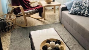Una sala de estar acogedora con un sillón mecedora, un sofá, una mesa de centro con un cuenco de bocadillos y una ventana con cortinas translúcidas.