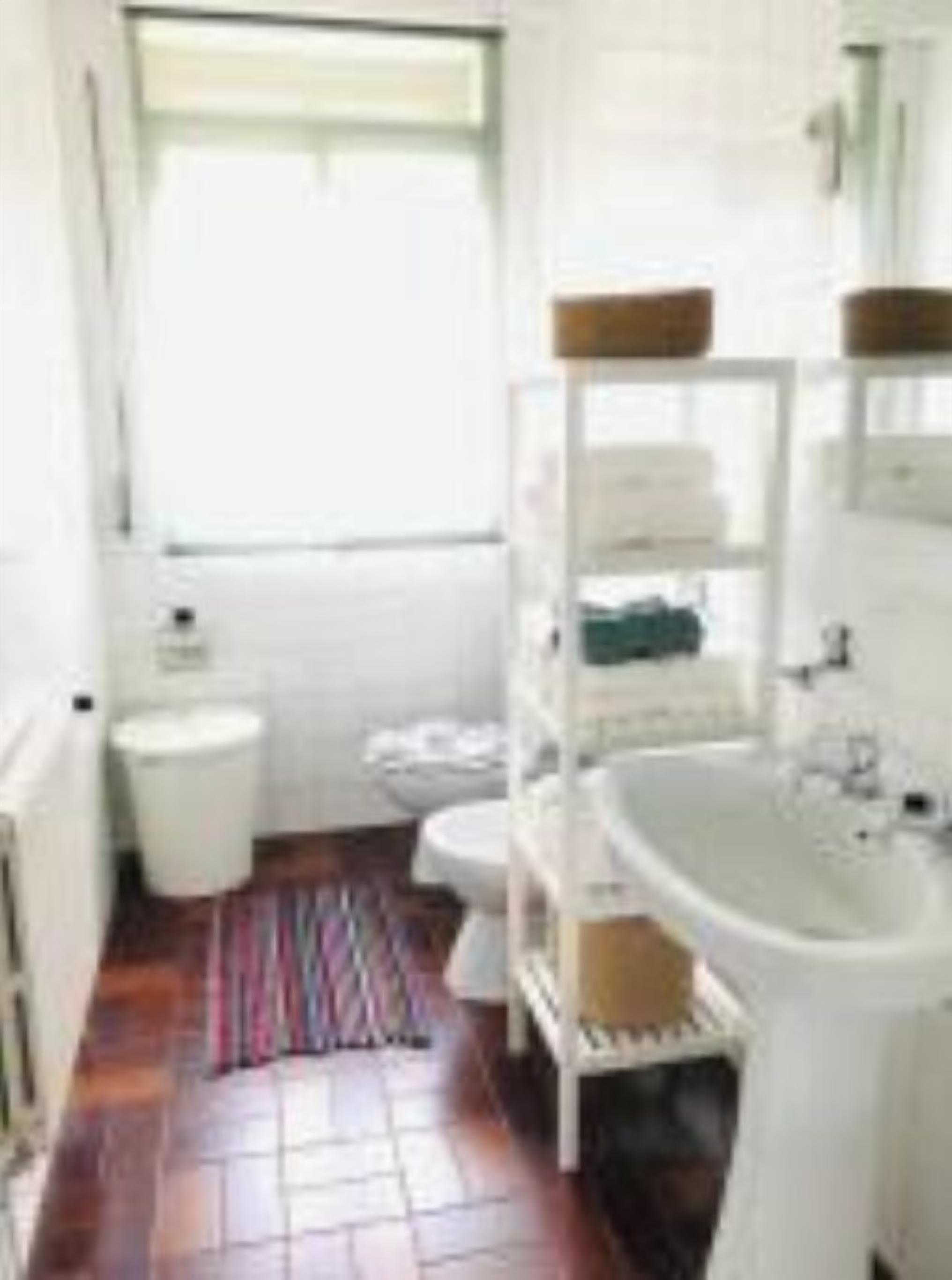 Et badeværelse med hvid vask, toilet og bruseområde. Der er et vindue, der giver naturligt lys.
