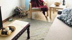 Una sala de estar acogedora con un sofá, una mesa de centro de madera, un sillón con una manta roja, una mesita con un farolillo y una cesta en el suelo.