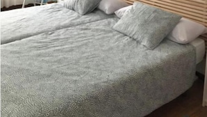 Una cama doble con cabecera de madera, ropa de cama gris y una silla blanca en una habitación con pared azul decorativa y una lámpara colgante.