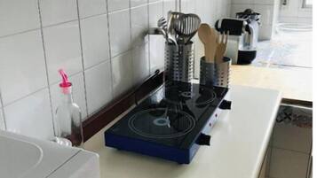 Una cocina con paredes de azulejos blancos, una estufa a gas, una cocina por inducción azul y varios utensilios en un recipiente.
