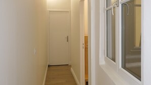 A narrow hallway with wooden flooring, white walls, and a door at the end.