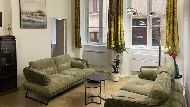 A living room with two green sofas, a small round table, a potted plant, and a painting on the wall.