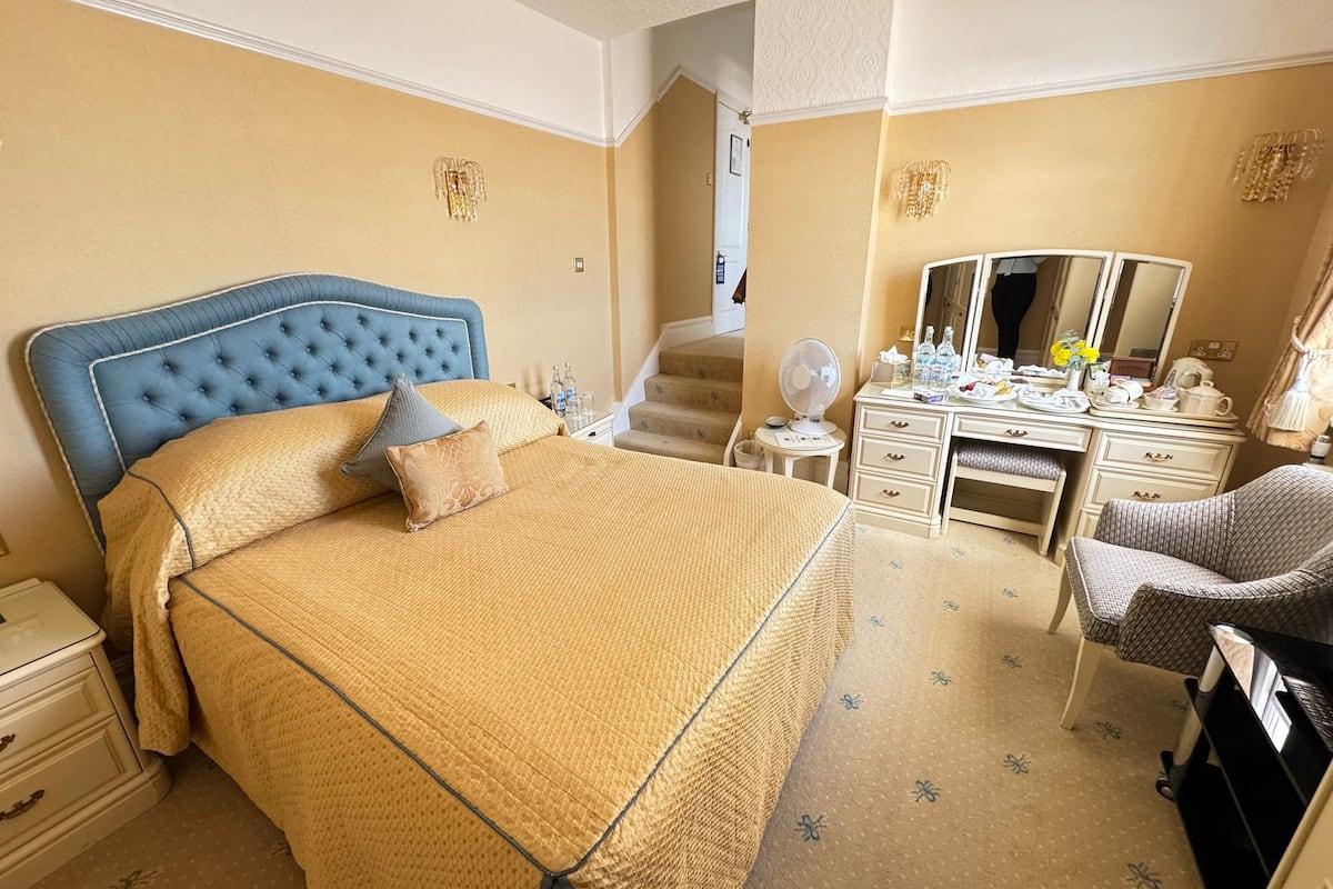 A hotel room with a large bed, a desk, a chair, a dresser, and a mirror.