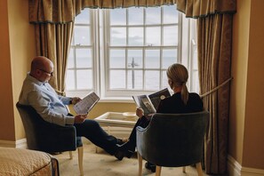 Deux personnes sont assises dans des fauteuils près d’une fenêtre, d’où l’on peut admirer la mer.