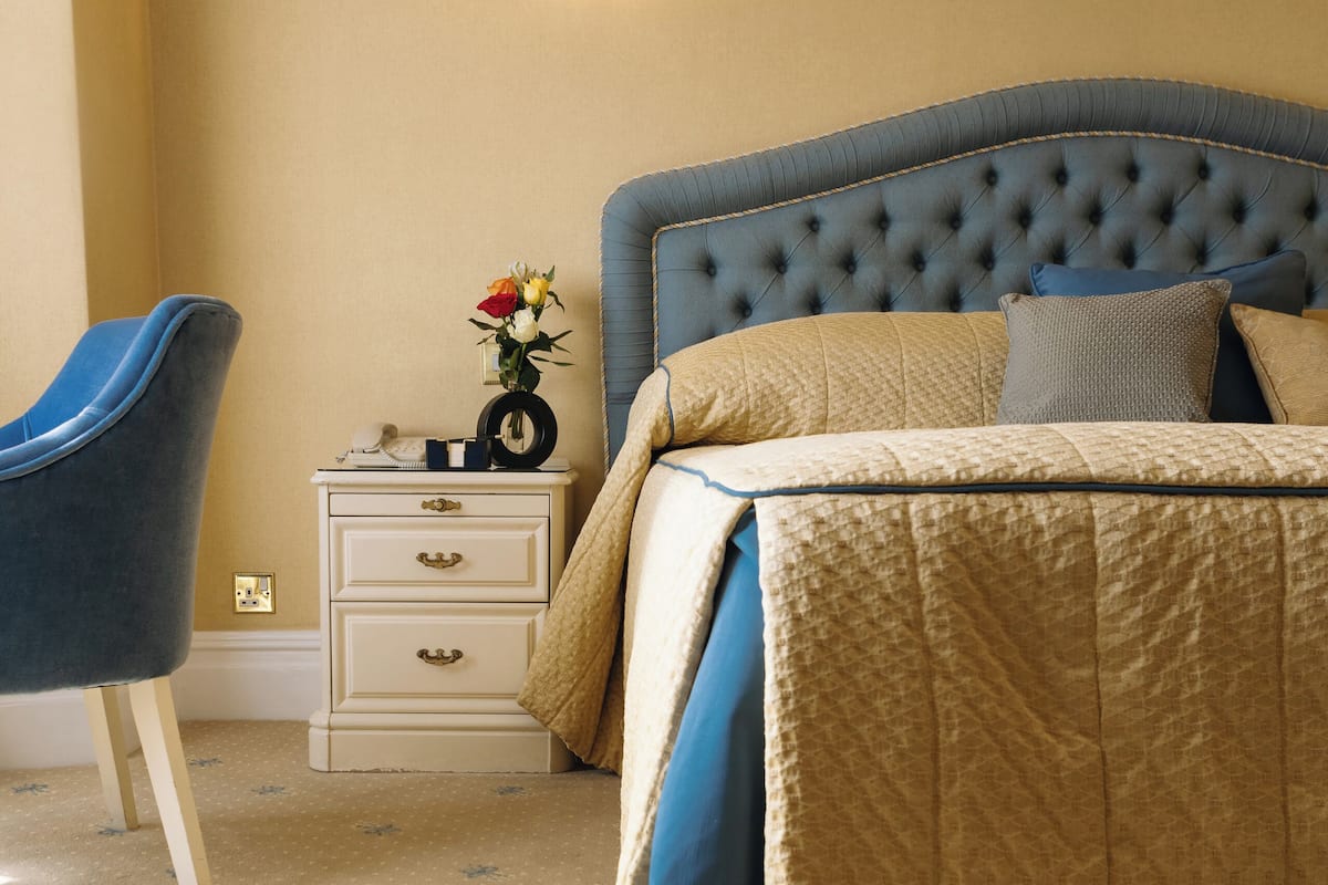 A bedroom with a tufted headboard, a bedside table with a vase of flowers, and a chair.