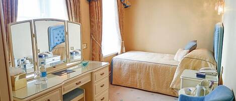 A hotel room with a bed, a desk with a mirror, a chair, and a bedside table.