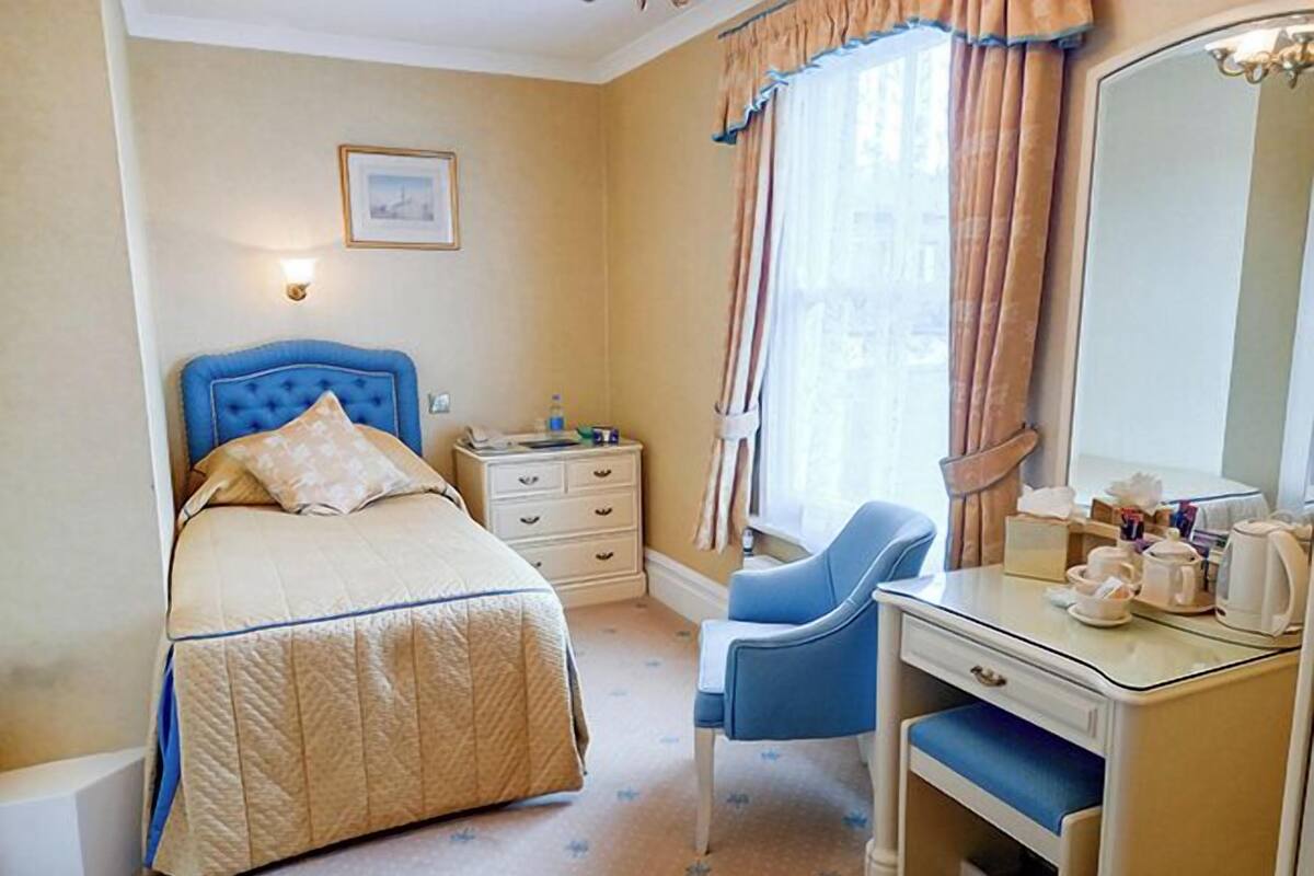 A bedroom with a bed, a desk, a chair, a dresser, and a mirror.