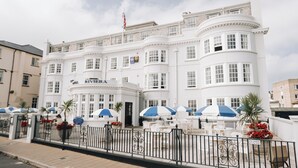 Un hotel blanco con fachada curva, mesas exteriores con sombrillas y una bandera en la parte superior.